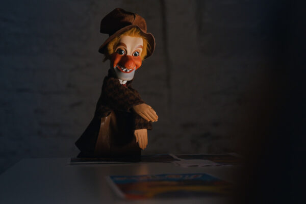 Une marionnette de Guignol, éclairée dramatiquement, regarde face caméra.